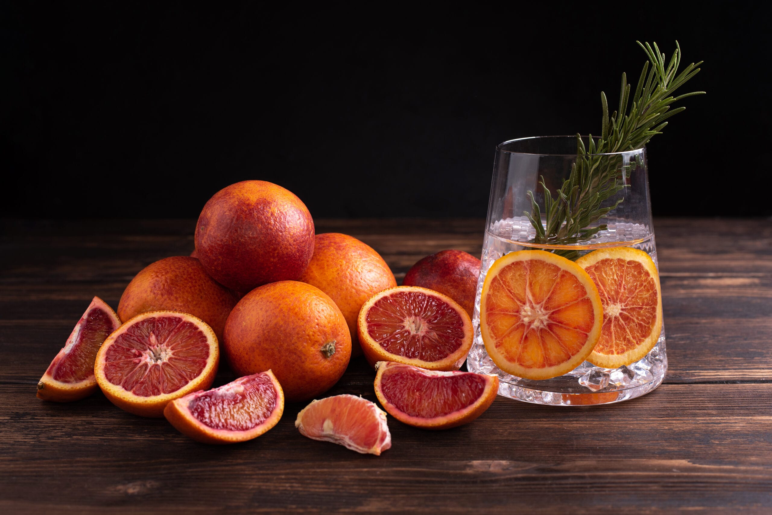 Blood Orange and Rosemary Gin presented in a glass tumbler. Blood orange fruits have been laid out on the table.