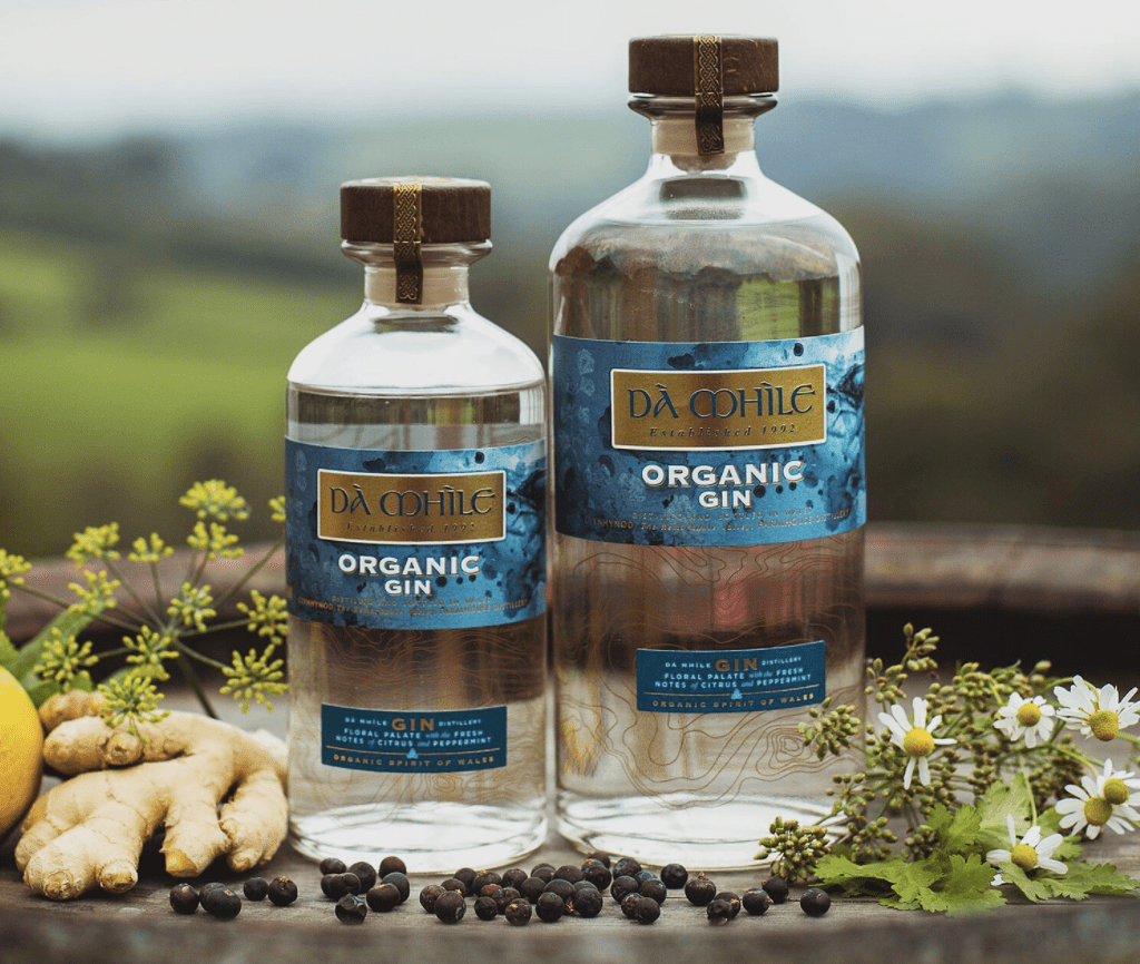 Two bottles of organic gin against a landscaoe of green rolling hills.